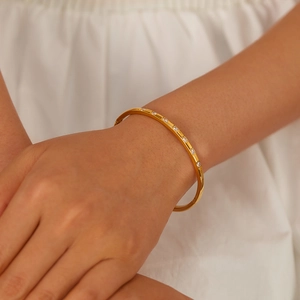 Detail shot of a slim gold stainless steel bangle with square zircon inlay on a wrist