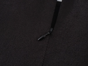 Détail d'une fermeture éclair invisible sur une robe noire à volants et texture croisée