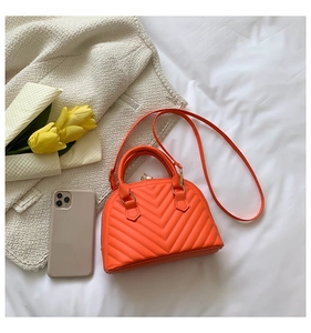 Close-up of bright orange shell bag with V-shaped quilting and sturdy top handles