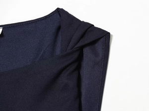 Detail view of the navy blue asymmetric dress featuring pleated neckline and shoulder knot