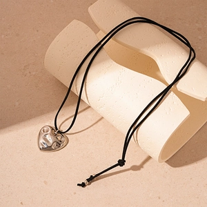 Macro detail of irregular liquid silver heart pendant on black cord over beige backdrop