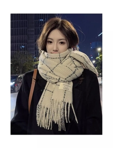 Close-up of beige plaid scarf with black stripes and fringe detail in outdoor night setting