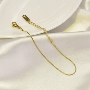 Close-up of 18K rose gold snake chain anklet with K18 hallmark on elegant beige silk