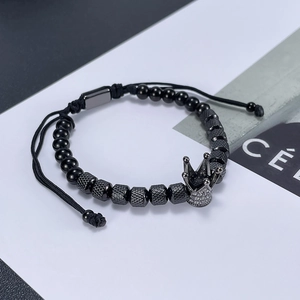 Detail view of black beaded bracelet featuring a sparkling zircon crown charm and adjustable knot