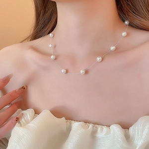 Détail d'un collier de perles blanches rondes sur le cou montrant un design perlé flottant