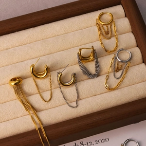 Detailed view of gold and silver tassel chain earrings in a wooden jewelry box display