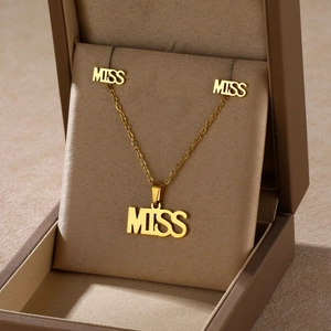 Detail shot of golden MISS script necklace and stud earrings set in a gift box