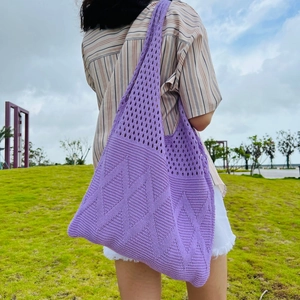 Outdoor shot of a large purple knit tote bag with geometric hollow patterns on a model