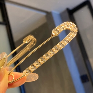 Macro shot of gold safety pin brooch with sparkling white pearls and rhinestones