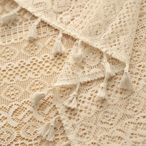 Close-up of beige lace fabric with hollow floral patterns and delicate fringe tassels