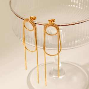 Details von goldenen Sicherheitsnadel-Ohrringen mit Schlangenkette-Quasten am Glas