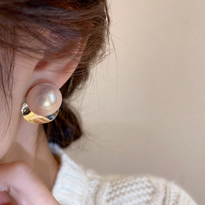 Close-up of a large pearlescent bead earring with golden metal base worn by a model
