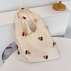 Close-up of red cherry embroidery on off-white canvas tote bag with textured fabric