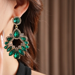 Détail de boucles d'oreilles de luxe avec émeraudes et glands dorés portés par un modèle