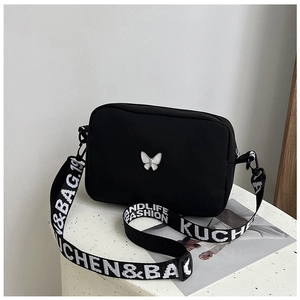 Detail of black nylon crossbody bag featuring white butterfly logo and lettered strap