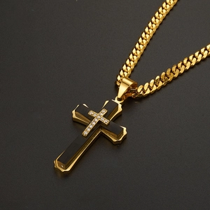 Macro shot of gold Cuban link necklace with black and gold cross pendant set with zircon