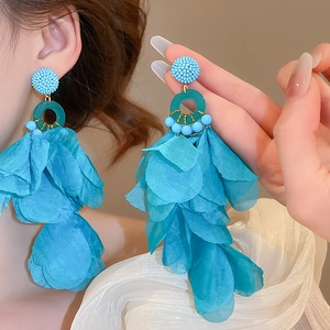 Detailed view of blue fabric petal flower earrings with beads worn by a model