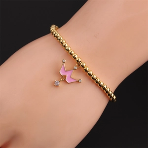 Détail d'un bracelet à billes dorées avec pendentif couronne en émail rose au poignet