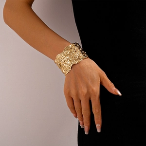 Close-up of a wide gold cuff bracelet featuring a unique wrinkled geometric texture