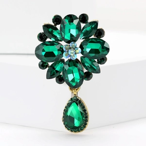 Macro shot of vintage gold brooch with green crystals and pear-shaped pendant detail
