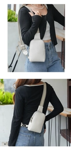 Detail of white leather chest bag showing dual silver zippers and striped fabric strap