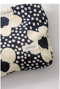 Close-up of dark blue floral makeup bag with cream flower pattern and woven H&R label