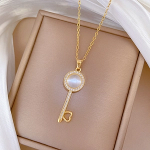 Macro view of gold key pendant necklace featuring a white opal stone and pavé crystal accents