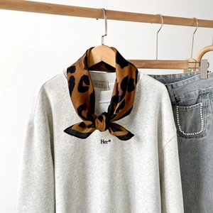 Detail eines Seidenschals mit Leopardenmuster an einem grauen Sweatshirt auf Holzbügel