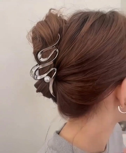 Silver wavy metal hair claw with pearl detail securing a dark brown bun hairstyle