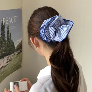 Blue and white striped fabric scrunchie with ruffled edges worn on a low ponytail
