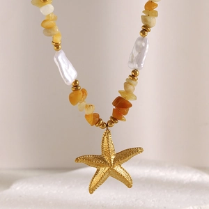 Detailed close-up of 18K gold starfish pendant with baroque pearls and orange gravel stones