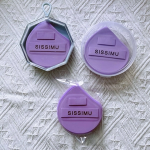 Three purple teardrop makeup sponges in clear packaging on a white woven background