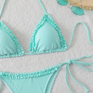 Flat lay of mint green striped bikini with ruffled edges, straw hat and sunglasses