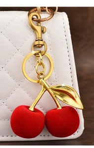 Detail of red flocked cherry keychain with gold leaves on a white quilted bag