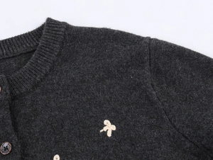 Close-up of knit cardigan showing dark grey wool fabric and beige bow embroidery