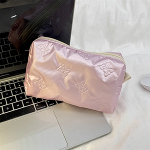 Detailed close-up of pink quilted satin cosmetic bag with butterfly pattern on laptop