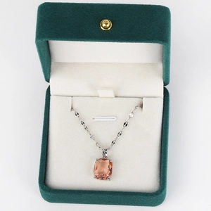 Close-up of a silver chain with orange rectangle gemstone pendant in green velvet box