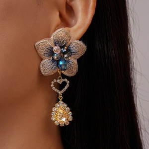 Détail macro de boucles d'oreilles fleur brodée asymétriques avec goutte ambrée