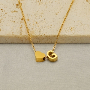 Polished gold stainless steel heart and letter G pendant necklace on stone background