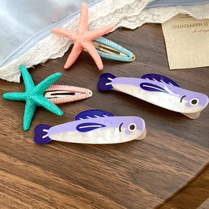 Close-up of four ocean-themed hair clips with starfish and fish designs on wood