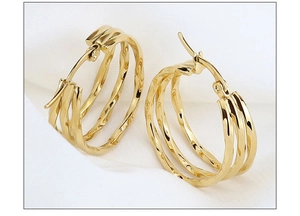 Macro detail of triple-layered golden steel hoop earrings on white silk fabric