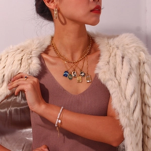 Close-up of layered 18K gold plated necklaces with tarot style pendants and pearl bracelet