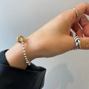 Detail of minimalist 925 sterling silver knotted ring and beaded bracelet on hand
