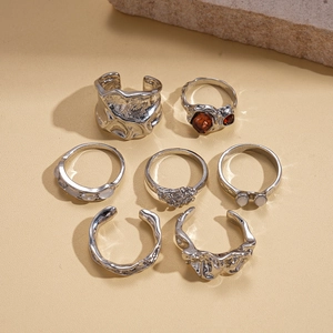 Detailed set of 7 textured metal rings with amber stones and pearls on stone base