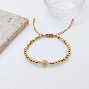 Detail of beaded gold bracelet with white daisy charm and adjustable beige cord