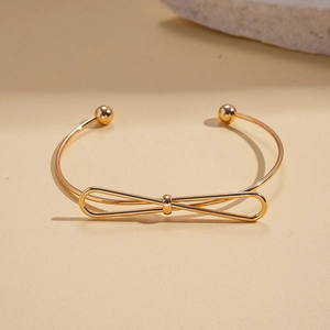 Close-up of a gold bow-knot open cuff bracelet with polished finish and spherical ends