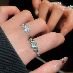 Close-up of a silver flower ring with light blue gemstone and zircon leaves on hand