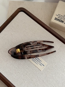 Detail view of large dark brown tortoiseshell hair claw clip with golden fashion engraving