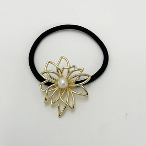 Detailed close-up of a black elastic hair tie with a golden flower and white pearl accent