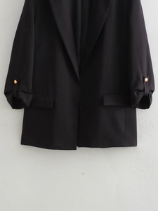 Detail of black blazer featuring notched lapels, rolled sleeves, and gold decorative buttons